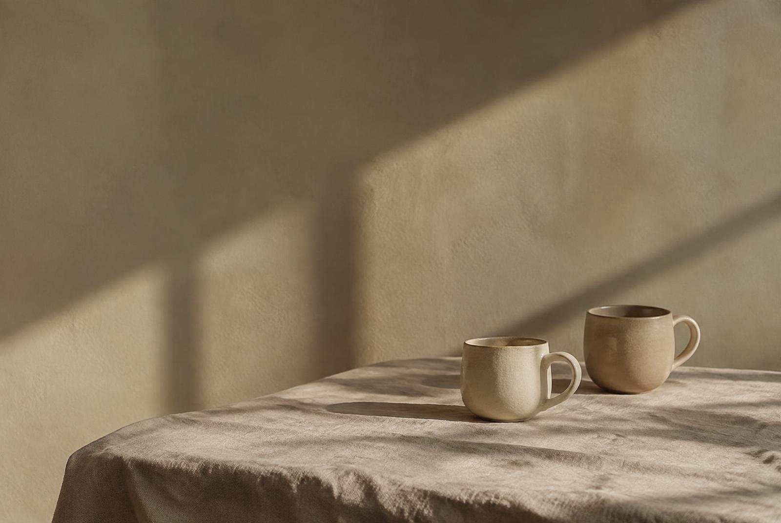 Deux tasses en céramique posées sur une nappe en lin, dans la lumière du soir